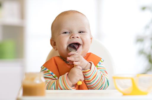 lachendes Baby mit Löffel im Mund